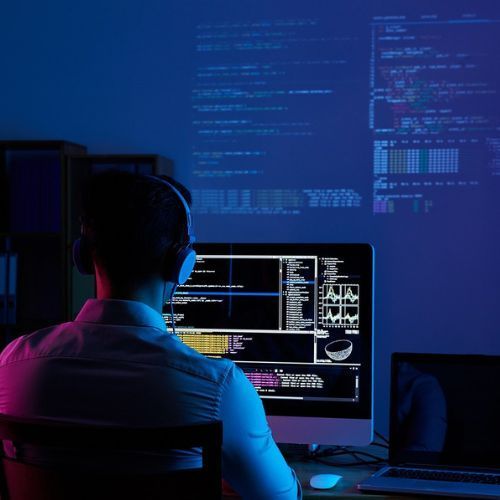 A man designs on his computer while code is also screened on the wall above him