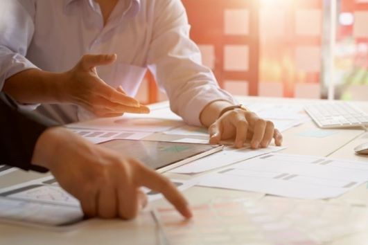 Two colleagues take part in strategic planning. The images focuses on their hands, the paperwork, an…