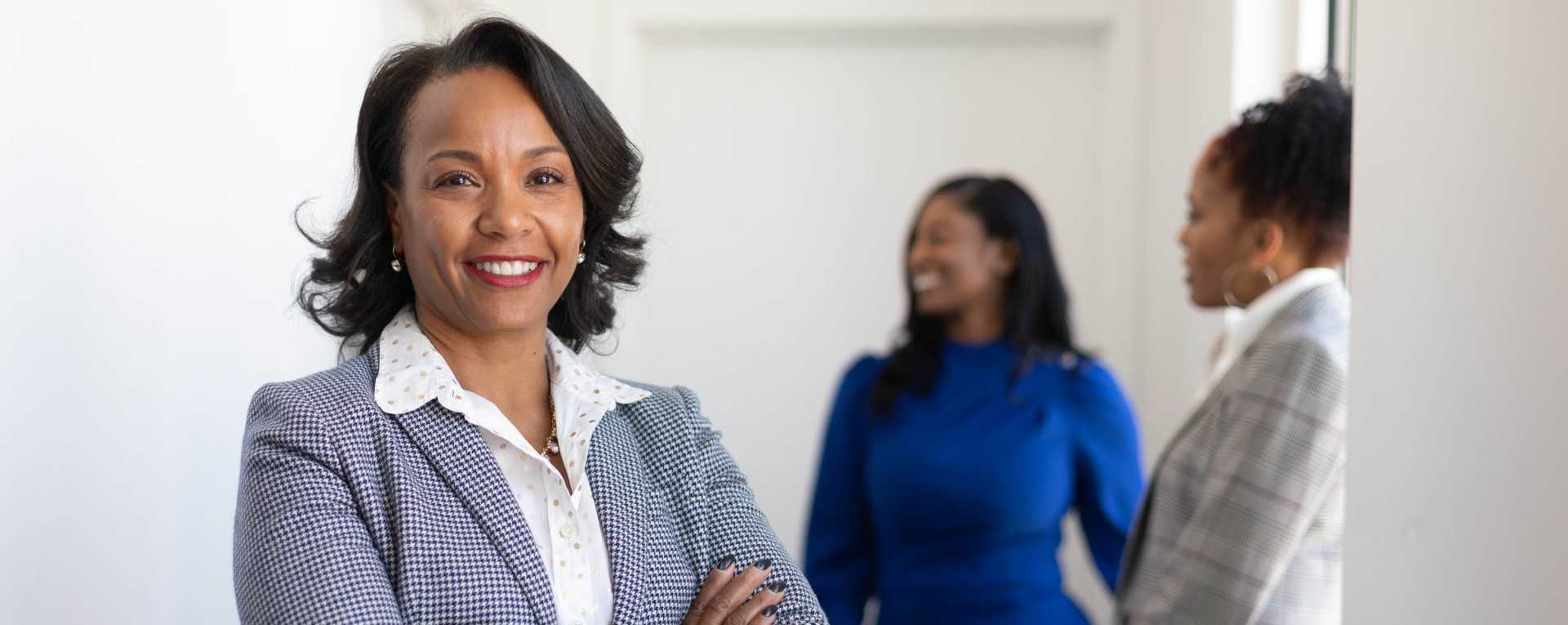 A Black woman with shoulder-length hair wearing black and white plaid sit smiles at the camera