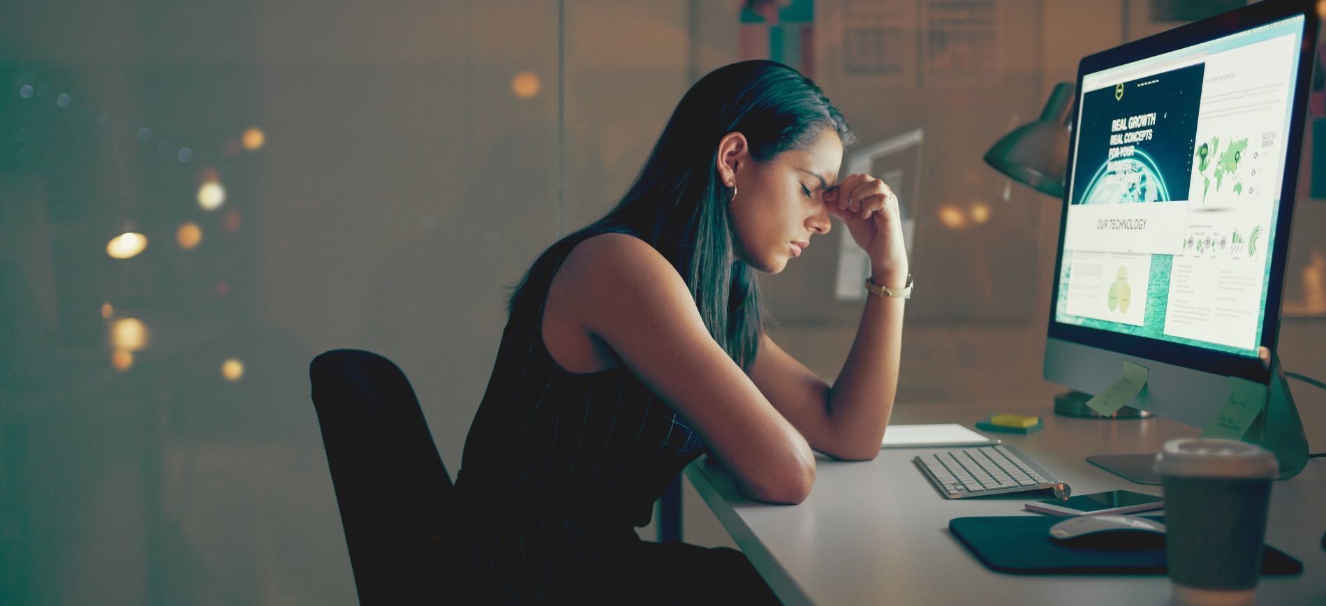 An exhausted woman sadly sits at her desk, rubbing to bridge of her nose