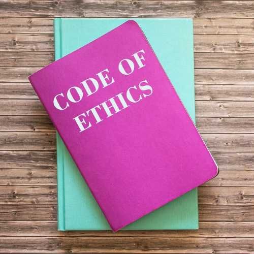 A pink Code of Ethics booklet sitting on a wooden desk