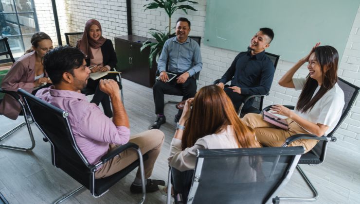 A diverse group of employees sit in a circle laughing