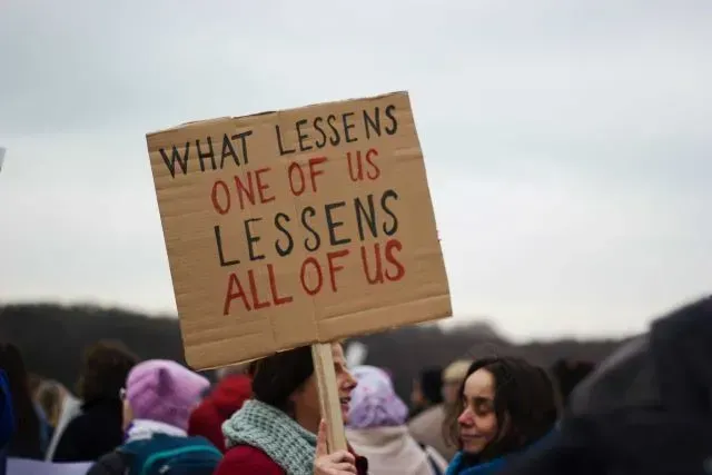 a group of protestors, one holding a sign that reads what lessens one of us lessens all of us