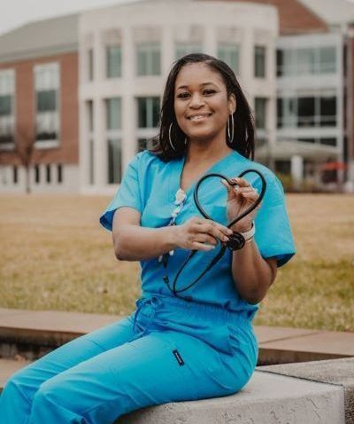 A Black female healthcare professional holds her stethoscope in the shape of a heart
