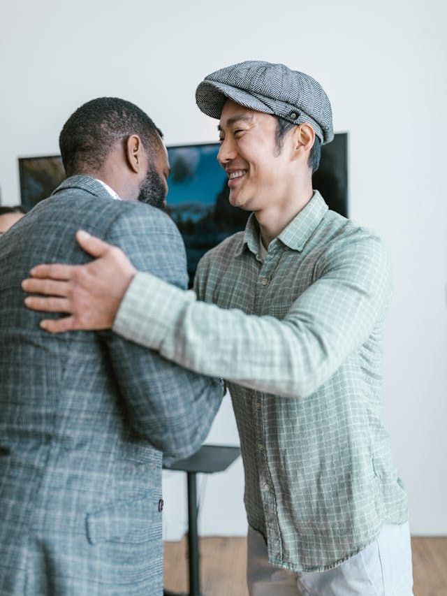 A Black man and an Asian man who are colleagues share a loose hug after a meeting