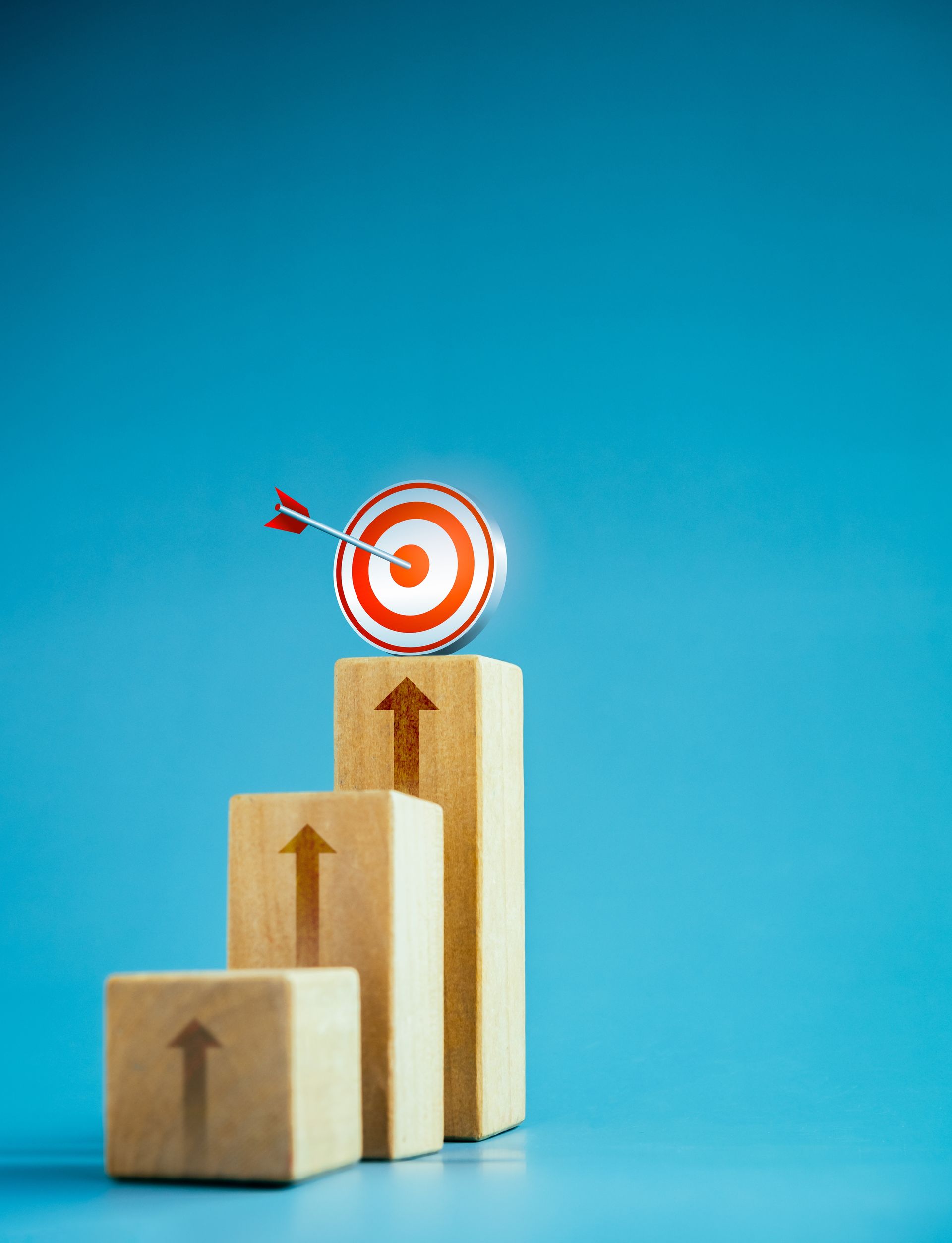 Three blocks in different sizes with arrows up painted on the blocks and directed towards a red and white target up top.