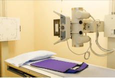 X-ray machine beside an examination table with a padded purple mat and pillow
