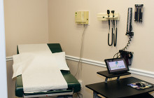 Exam room with exam table, wall-mounted medical tools, and a laptop on a cart