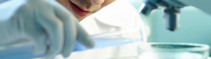 Lab technician in blue gloves handling a petri dish under a microscope in a bright laboratory