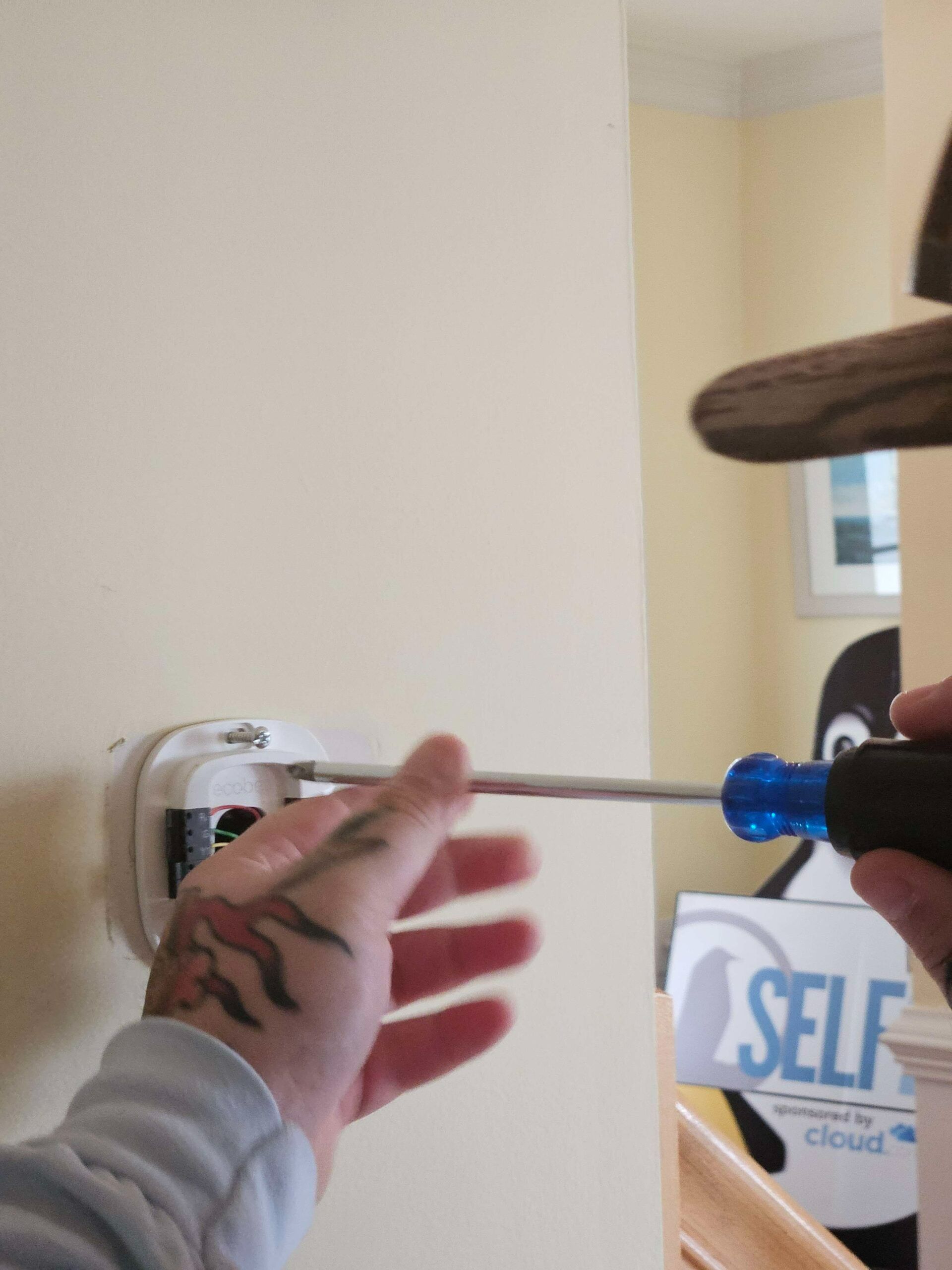 Hand using a screwdriver to adjust a wall-mounted device in a room
