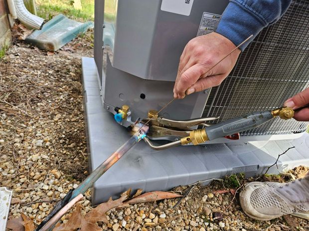 Technician connecting a torch and hoses to an outdoor HVAC unit during maintenance