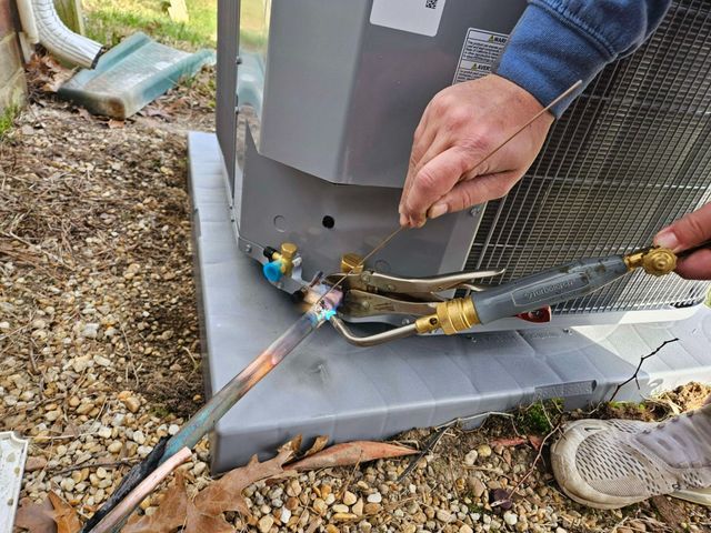 Technician connecting a torch and hoses to an outdoor HVAC unit during maintenance