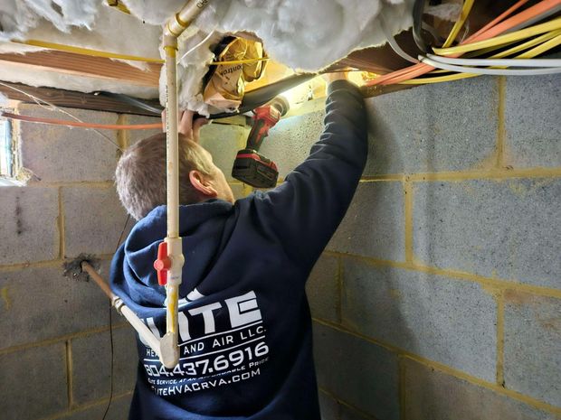 Worker installing wiring in a crawlspace, reaching up near insulation and cinder block wall.