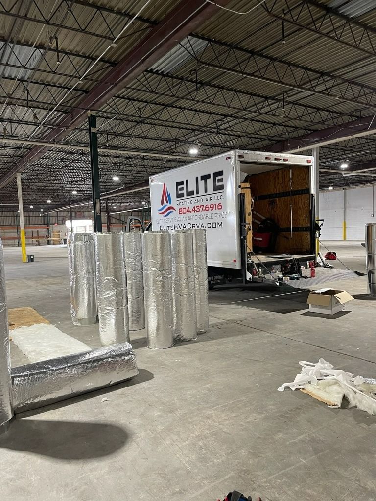 Warehouse loading dock with an Elite Movers truck, stacked items, and wrapped materials on the floor.