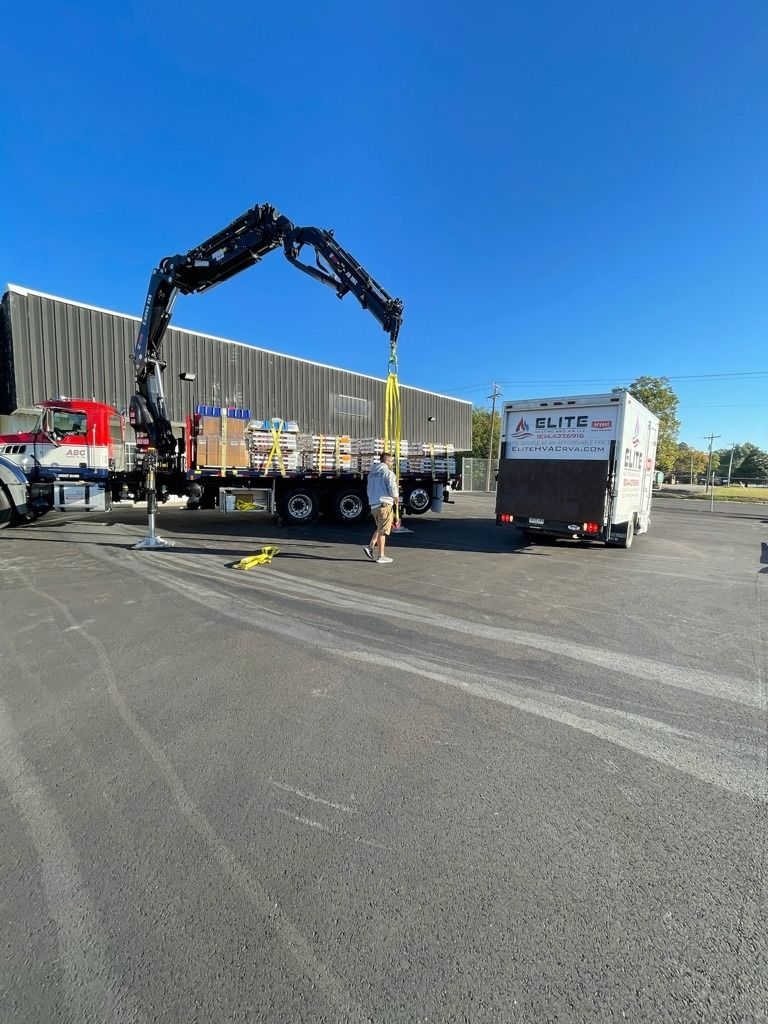 Construction truck with boom crane lifting materials beside a warehouse on a sunny day