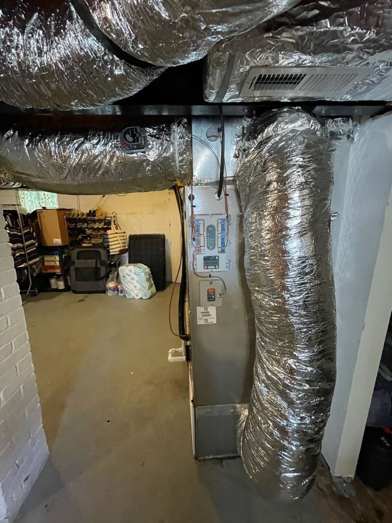 Basement with large insulated HVAC ducts and a furnace unit beside storage shelves.