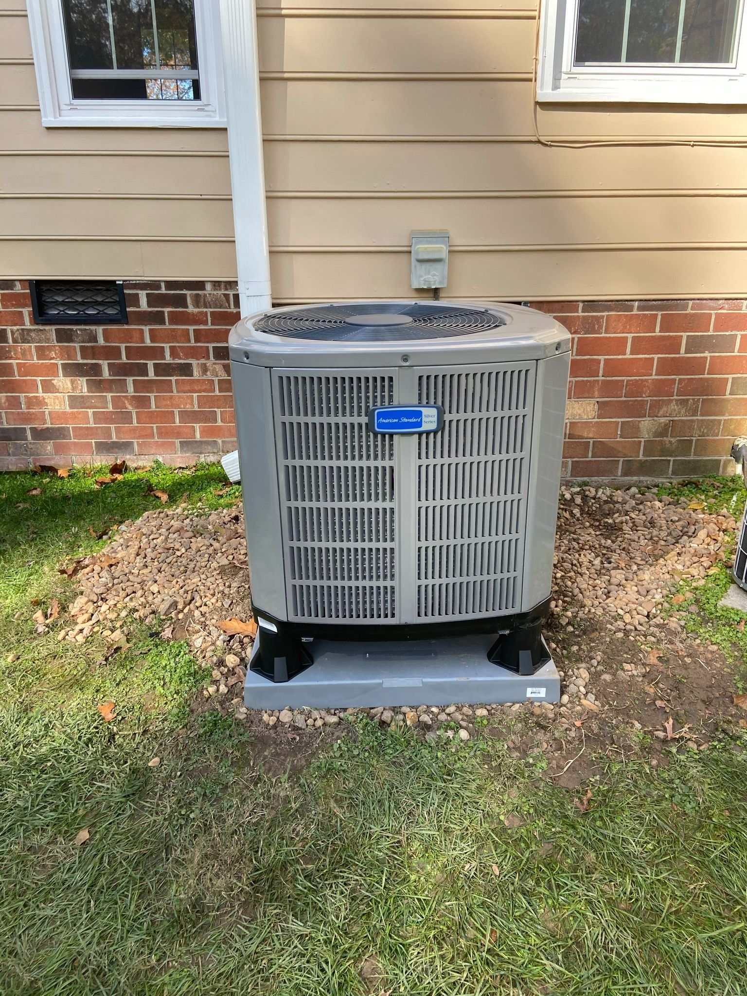 Outdoor HVAC unit on a grassy lawn beside a beige house with brick trim.