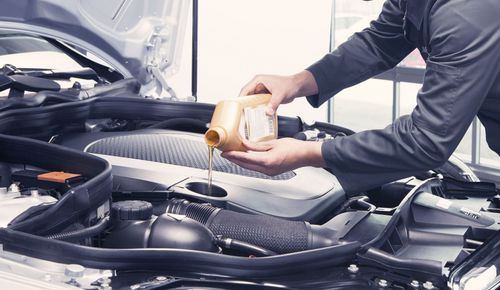 Person pouring oil into a car engine in a garage.