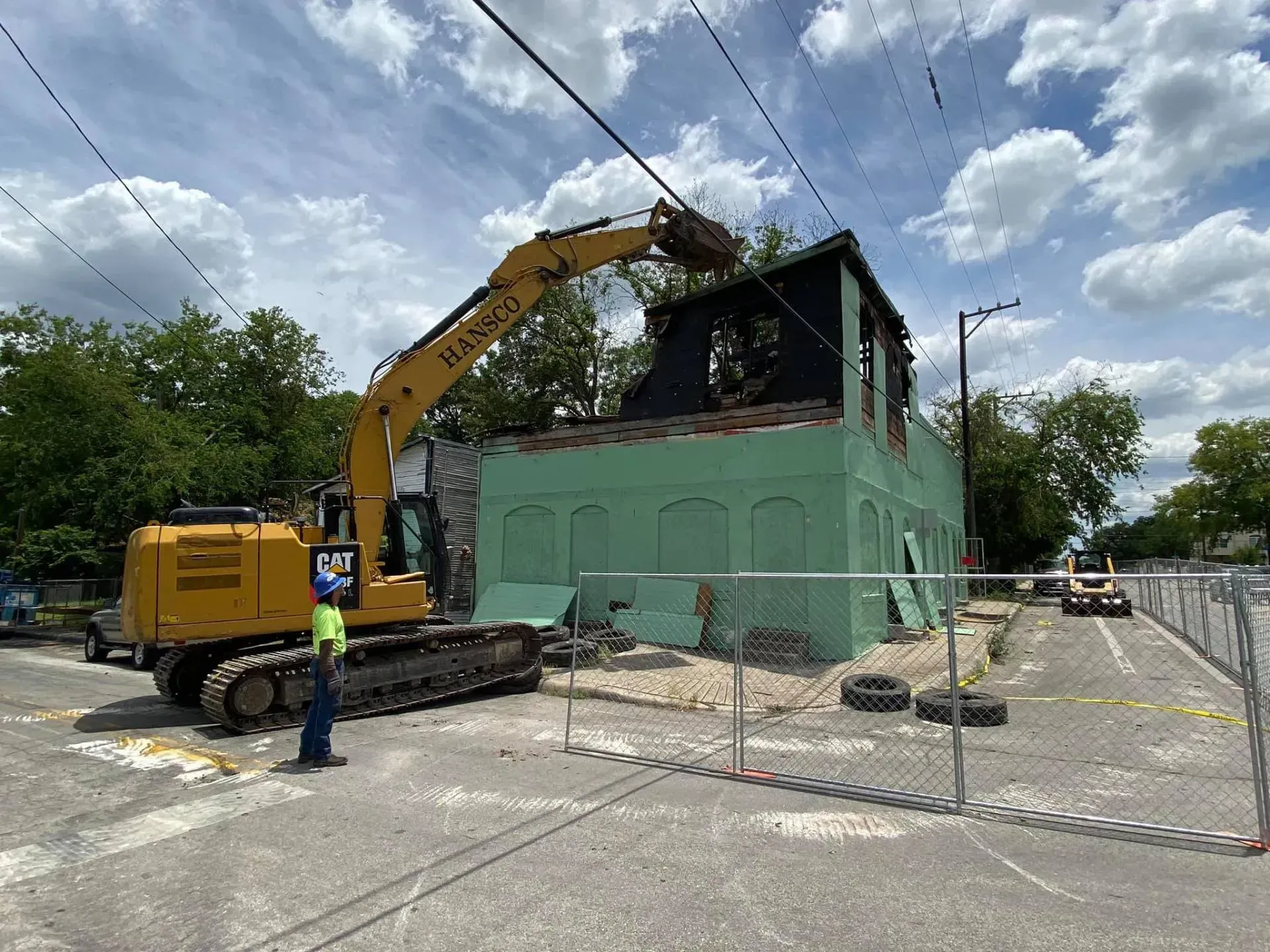 Demolition of a green building with excavator; utility lines overhead.