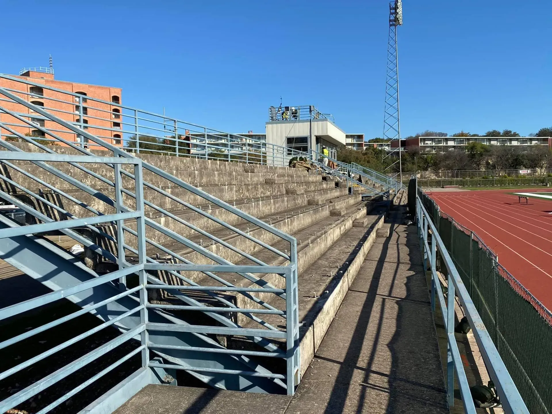 Bleachers at a track and field stadium, with blue railings and a control booth.