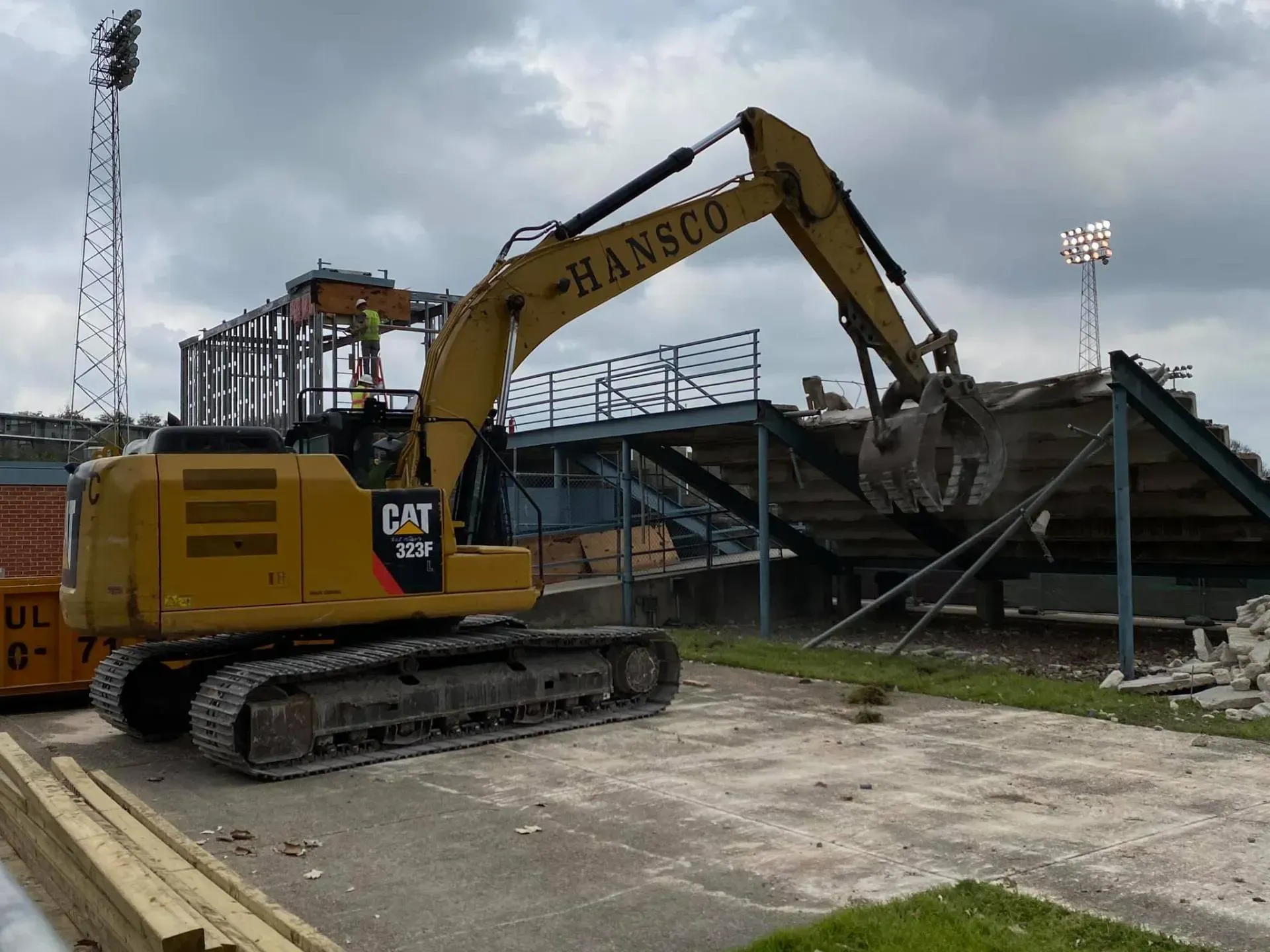Yellow excavator demolishing stadium bleachers; HANSCO logo visible.
