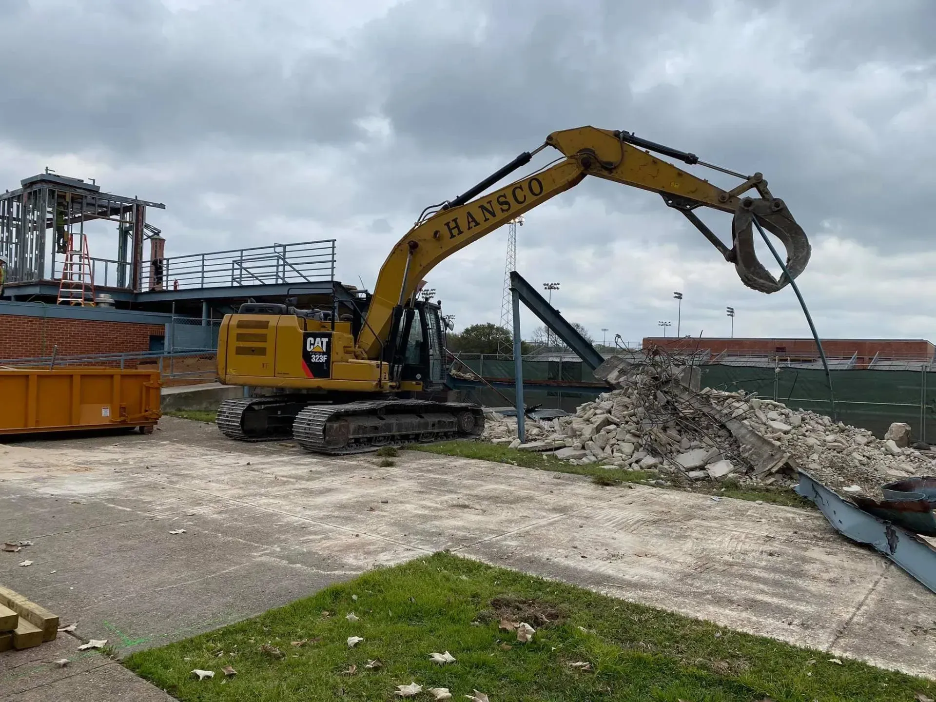 Yellow excavator demolishing a structure on a cloudy day; concrete rubble on the ground.