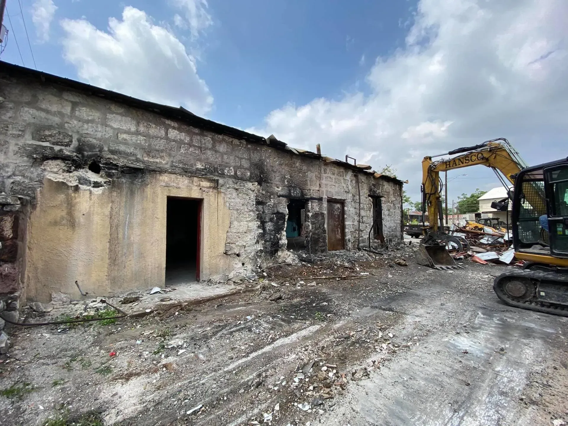 Damaged building, dark patches from fire, with excavator in the background, demolition taking place.