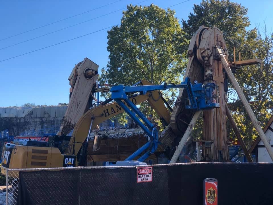 Demolition of amusement park ride, excavator and lift present. Trees and blue sky visible.