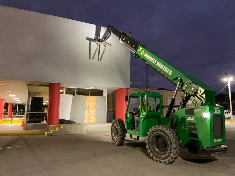 Green telehandler near a building, loading construction materials.