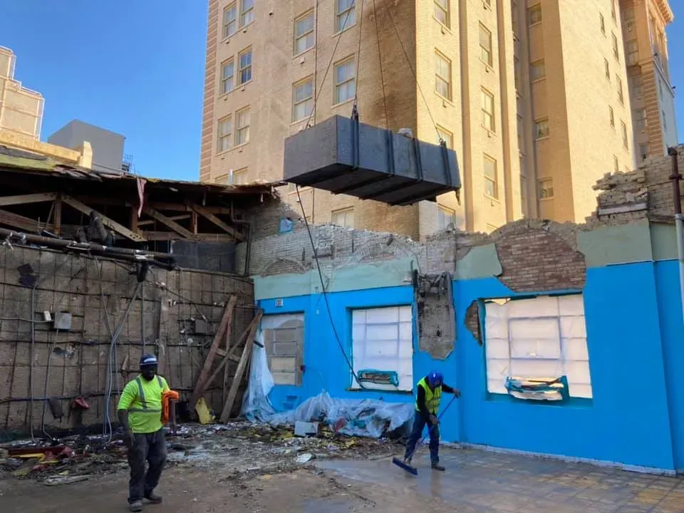 Construction site: Demolition of a building. Workers and crane lifting a large block.