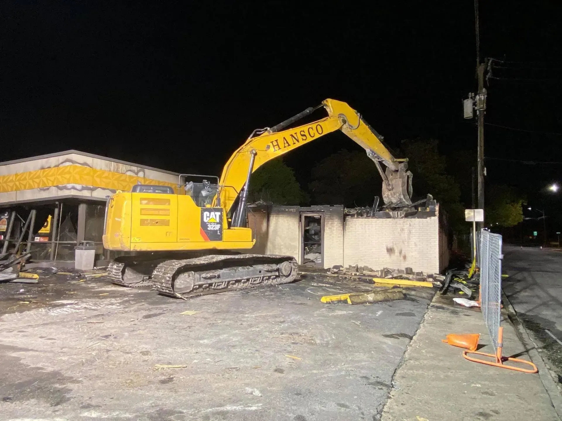 A yellow excavator demolishes a burnt building at night.