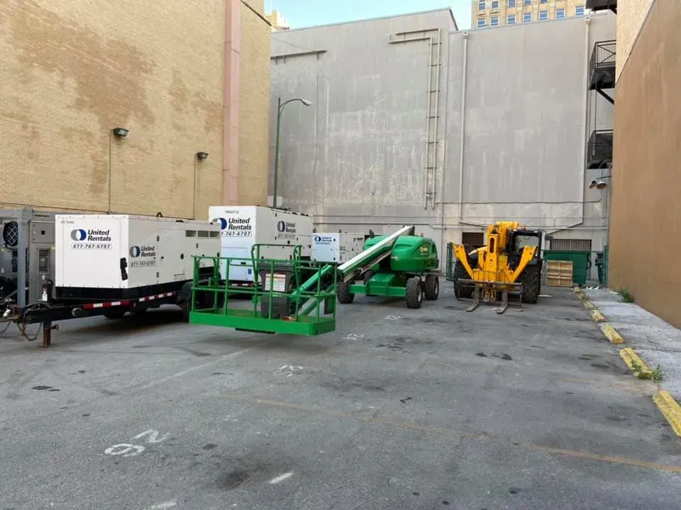 An alleyway with construction equipment. Generators, a lift, and a forklift stand in a paved area between buildings.