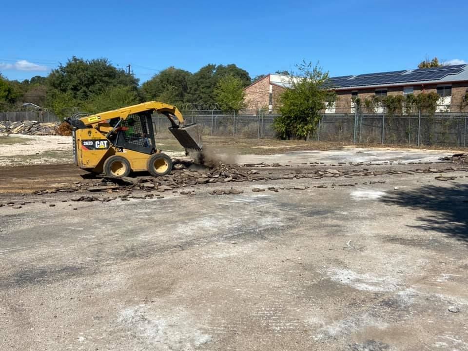 Yellow CAT skid steer demolishing a brick surface on a sunny day.