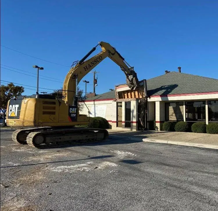 Yellow excavator demolishing a building on a sunny day.