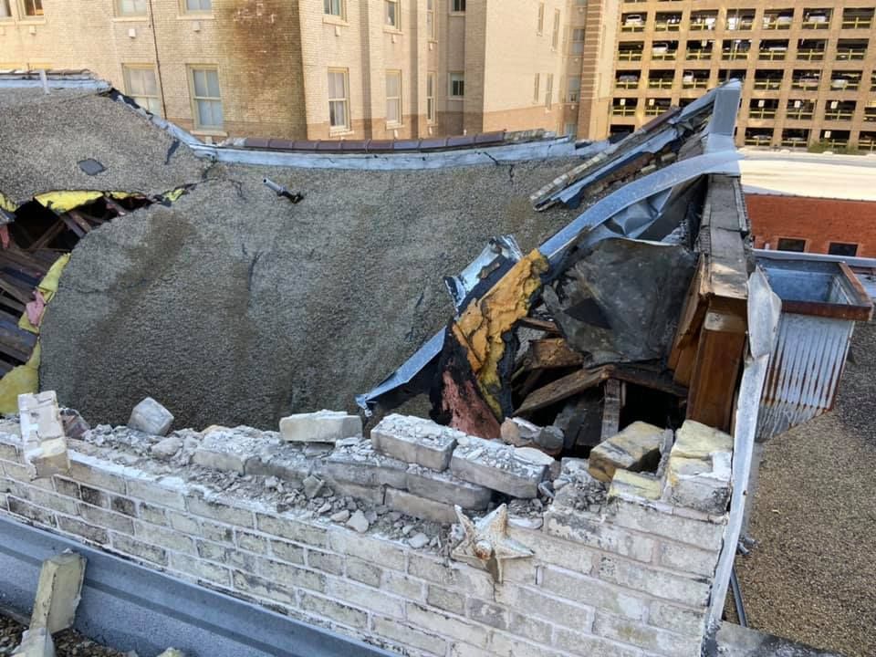 Damaged roof of a building, showing collapsed sections, bricks, and debris.