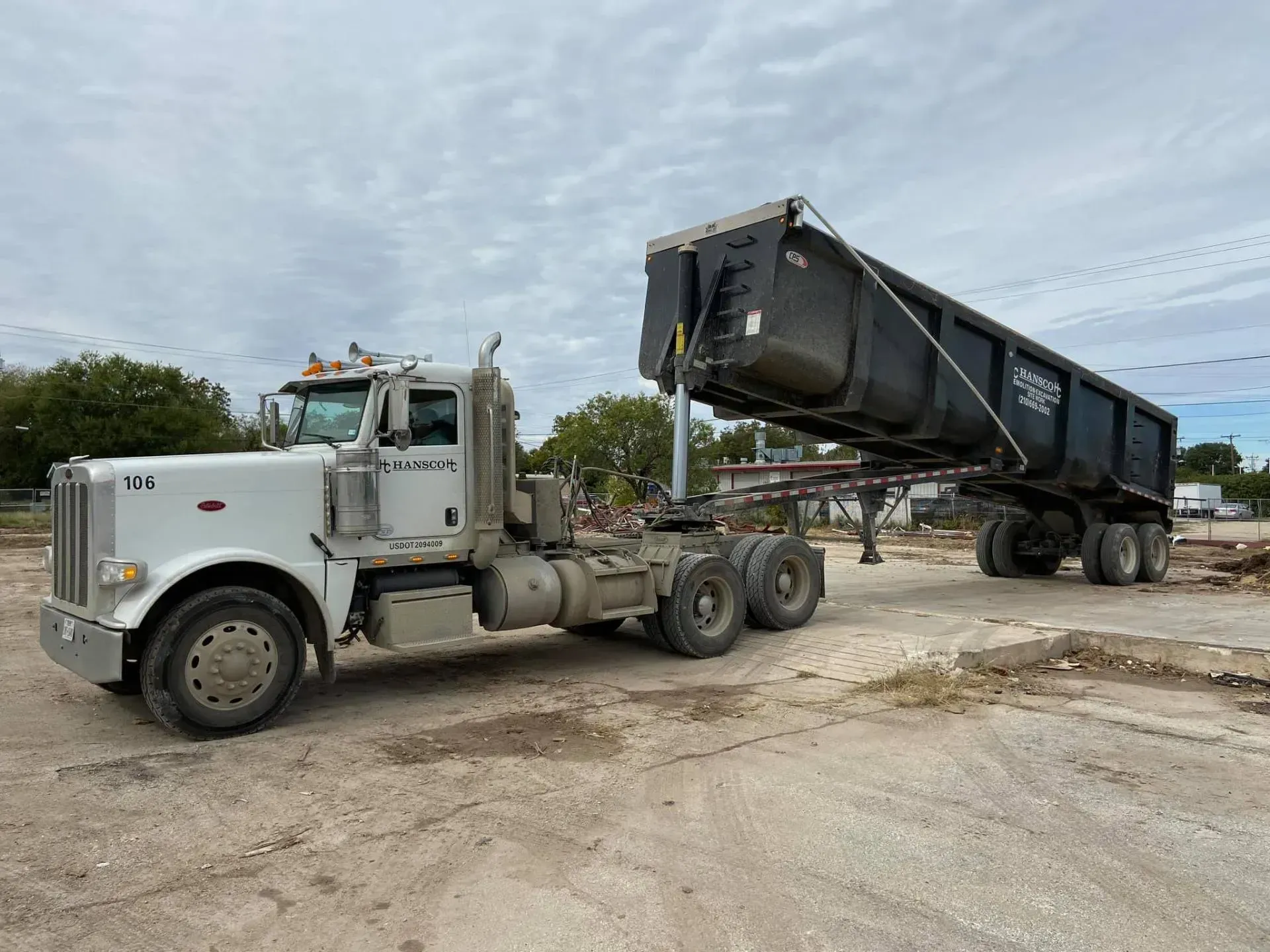 White dump truck with raised trailer on a gravel surface under a cloudy sky.