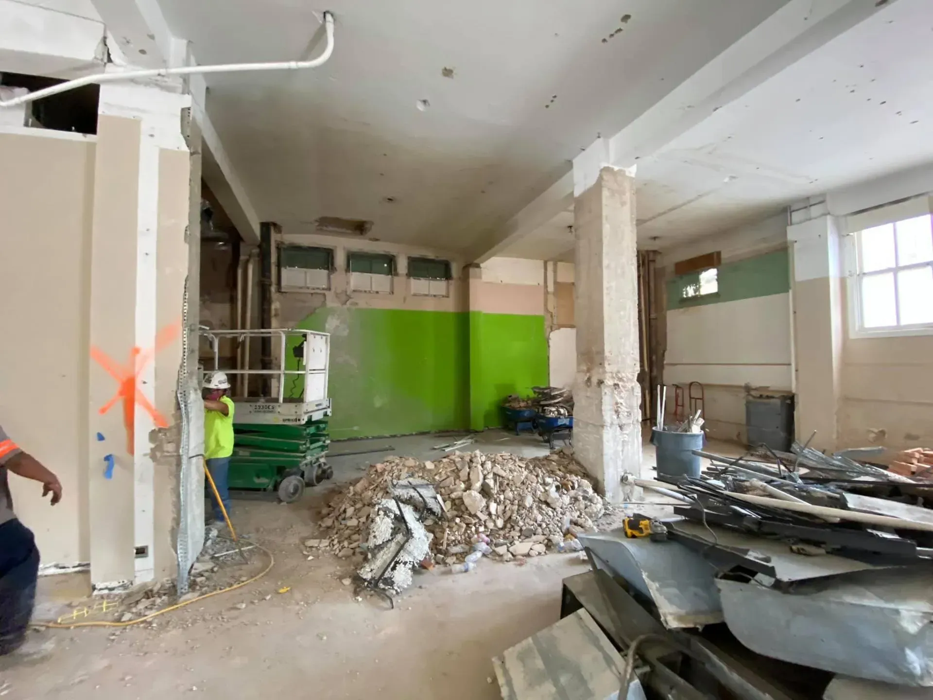 Interior demolition site with debris, green wall, worker, and construction materials.