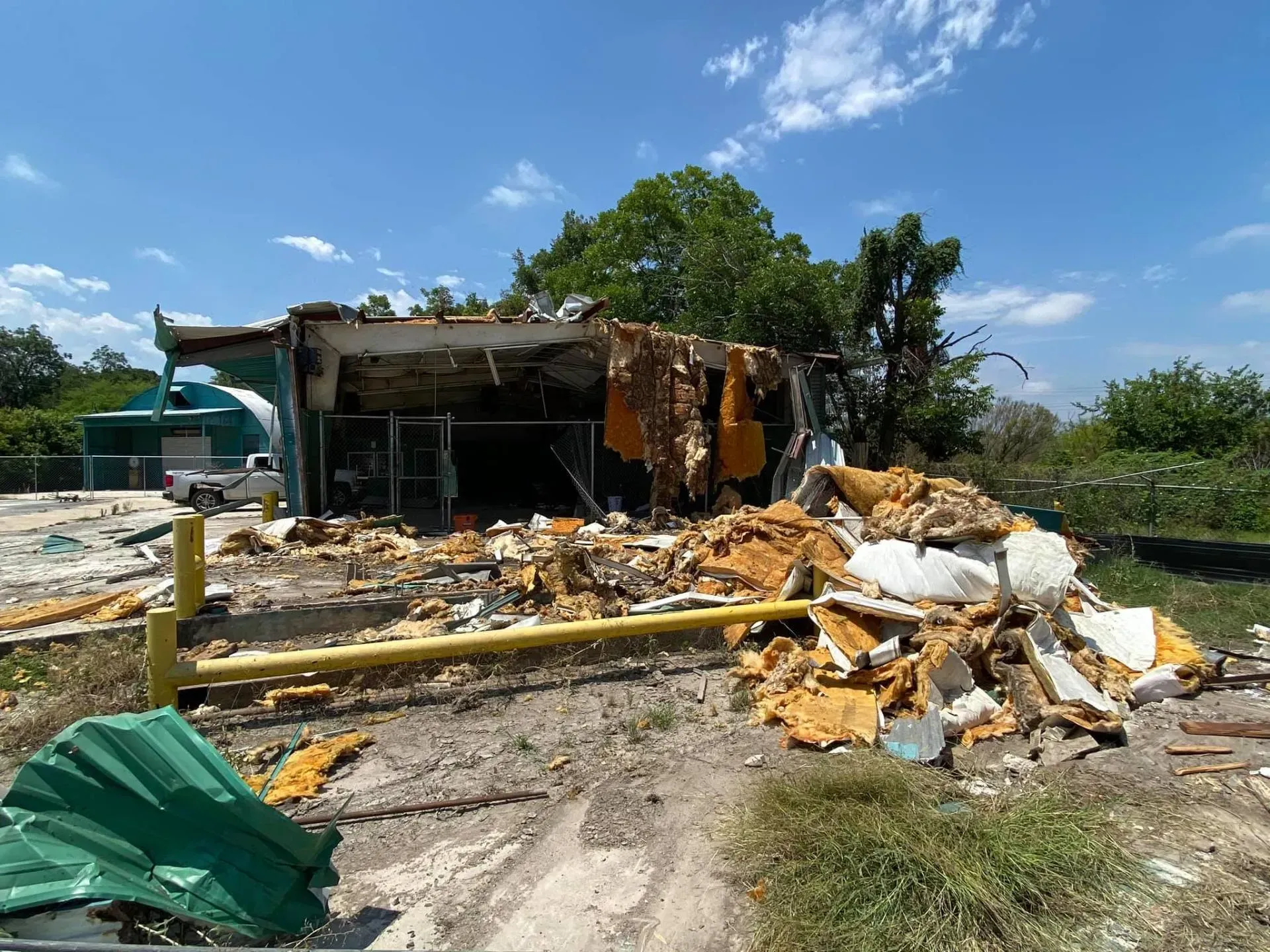 Destroyed building with debris; blue sky, sunny day.