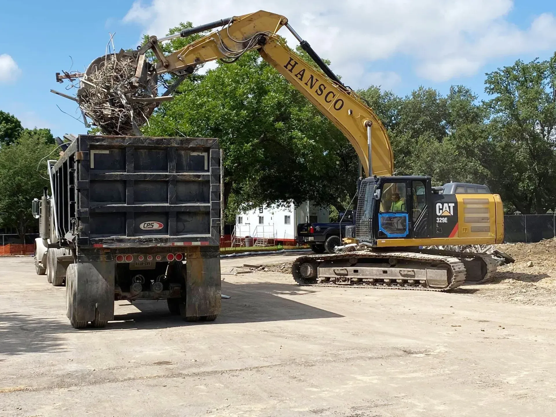 Yellow excavator loading debris into a black dump truck at a construction site.