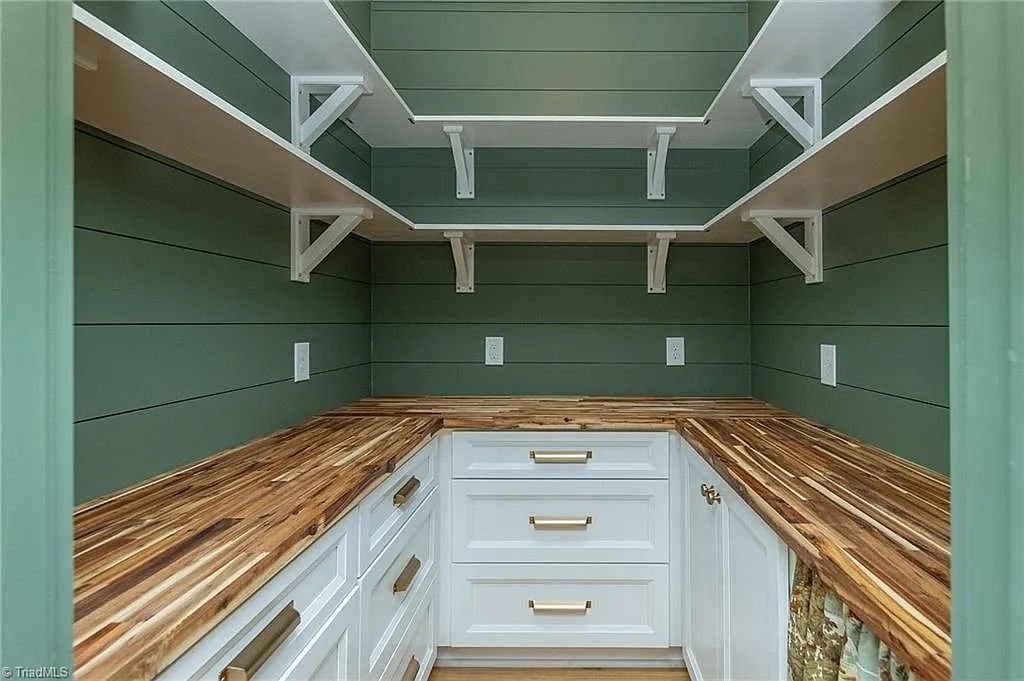 Green pantry with white shelves, cabinets, and wood countertops; brass handles.