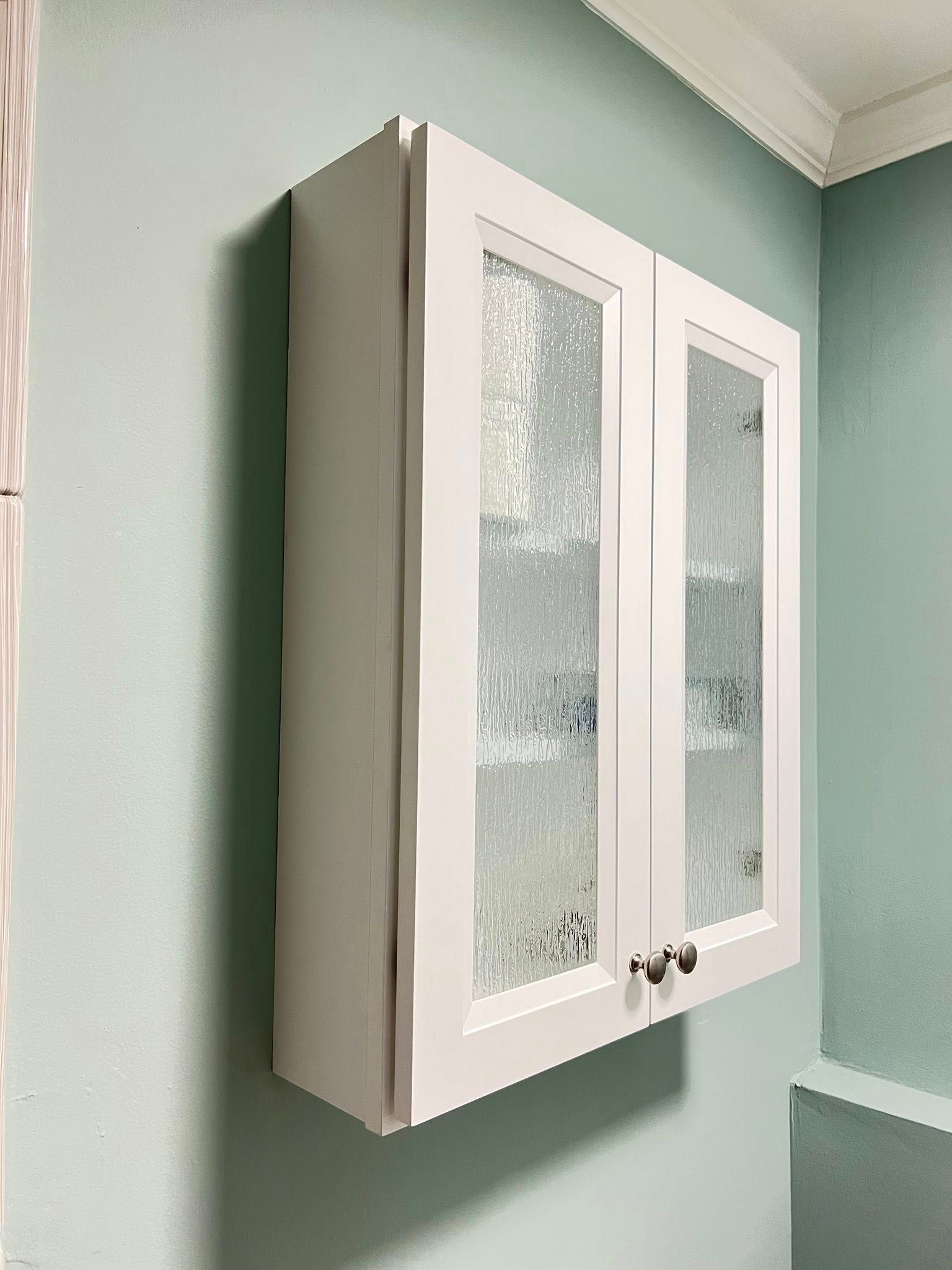 White cabinet with frosted glass doors mounted on a light blue wall.