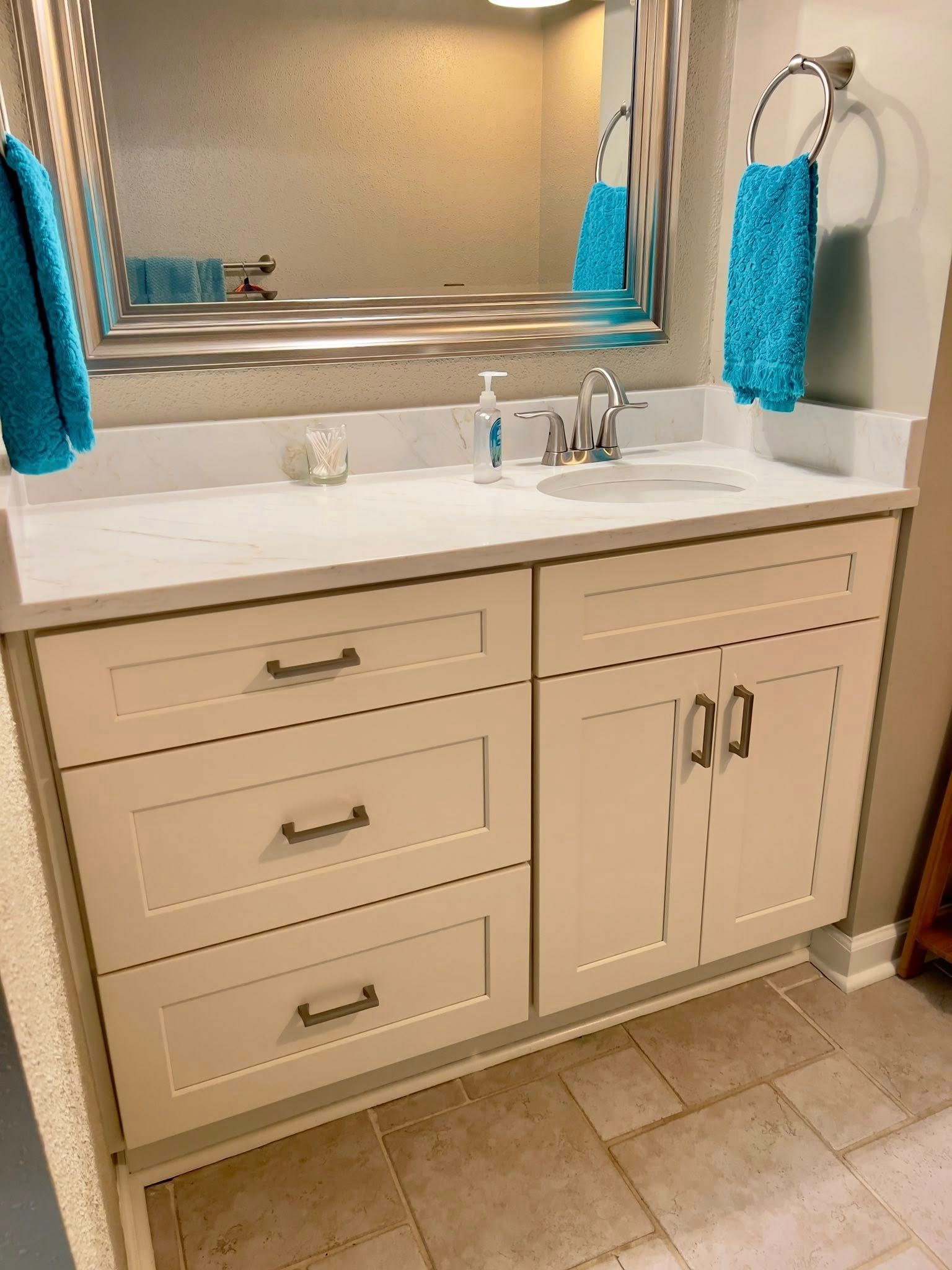 Bathroom vanity with beige cabinets, white countertop, and turquoise towels.