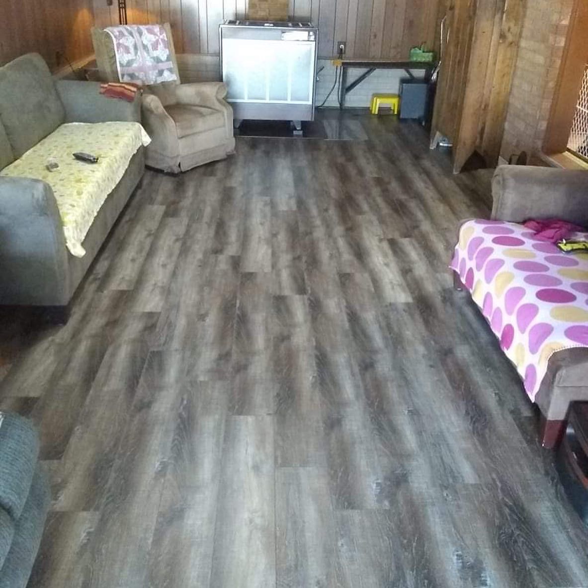 A living room with gray wood-look flooring, multiple couches, and an air conditioner.