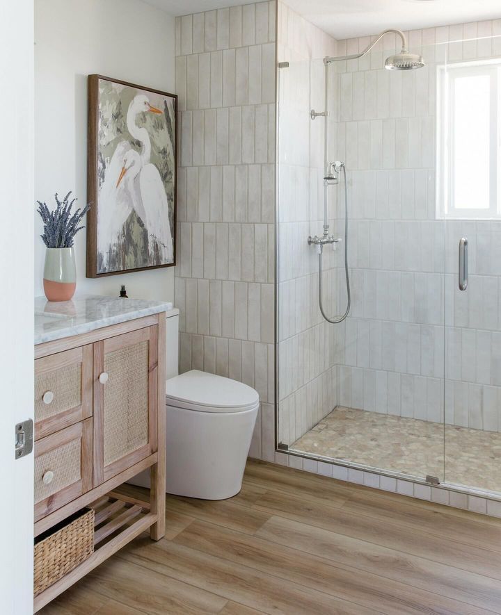 Bathroom with shower, wood-look flooring, light-colored tile, vanity with art, and a white toilet.