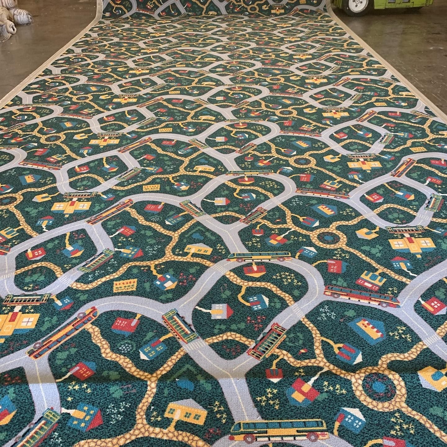 Road map rug with green, yellow, and red buildings, grey roads, and green trees.