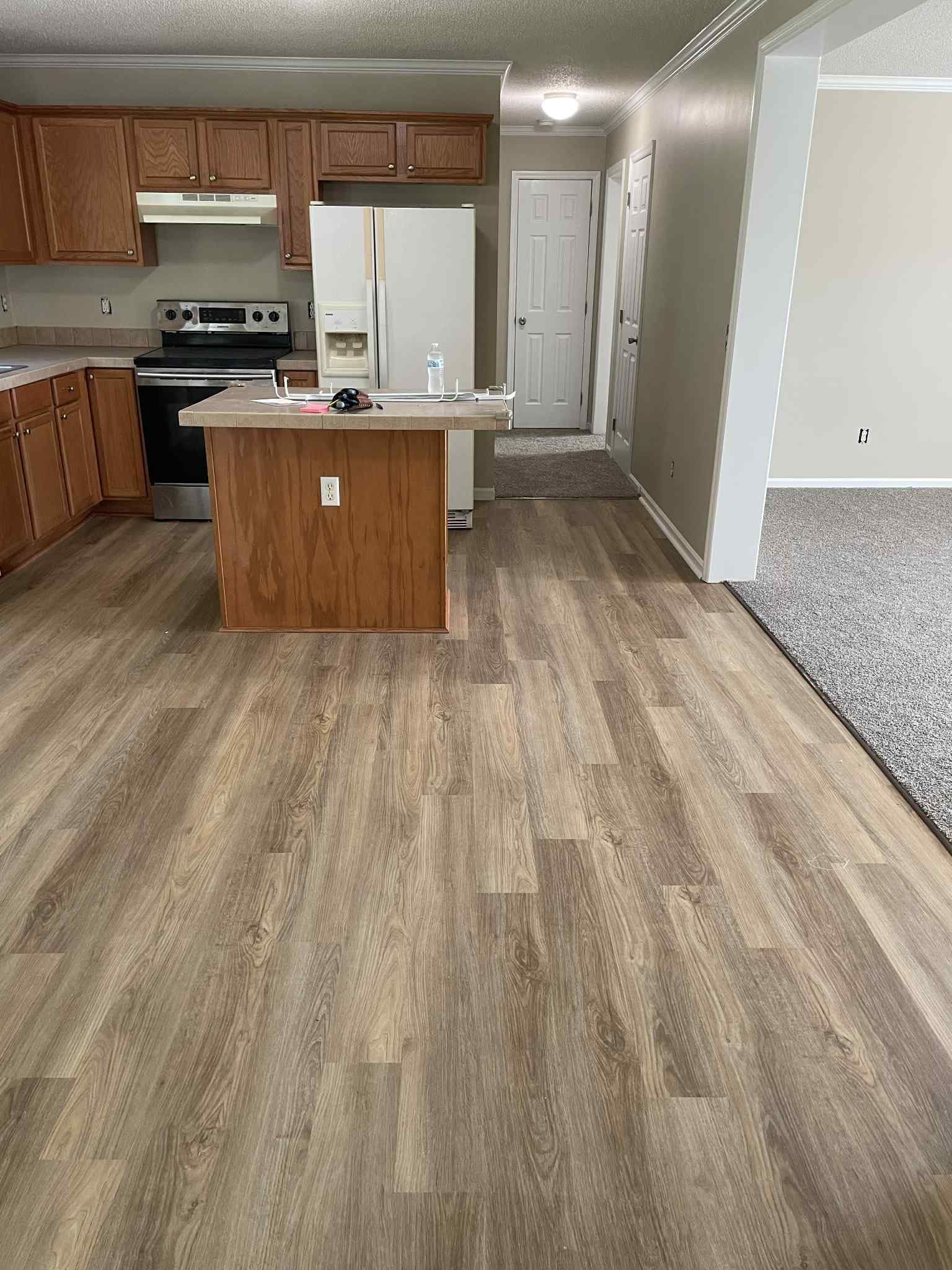 Kitchen with wood-look flooring, cabinets, island, and appliances. A doorway leads to a hallway.