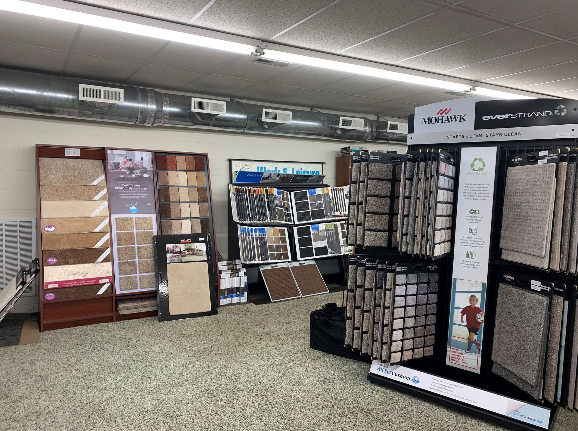 Carpet samples on display in a retail store. Brown, tan, and gray swatches are shown on racks and panels.