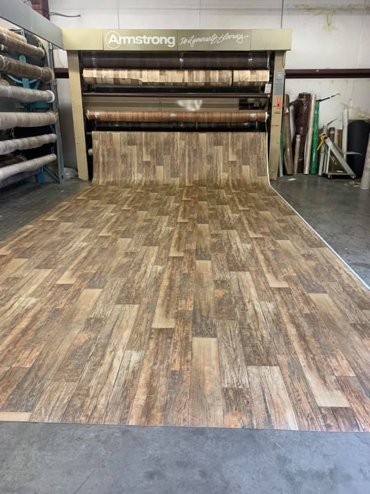 A roll of wood-look flooring being unrolled from a machine in a warehouse.