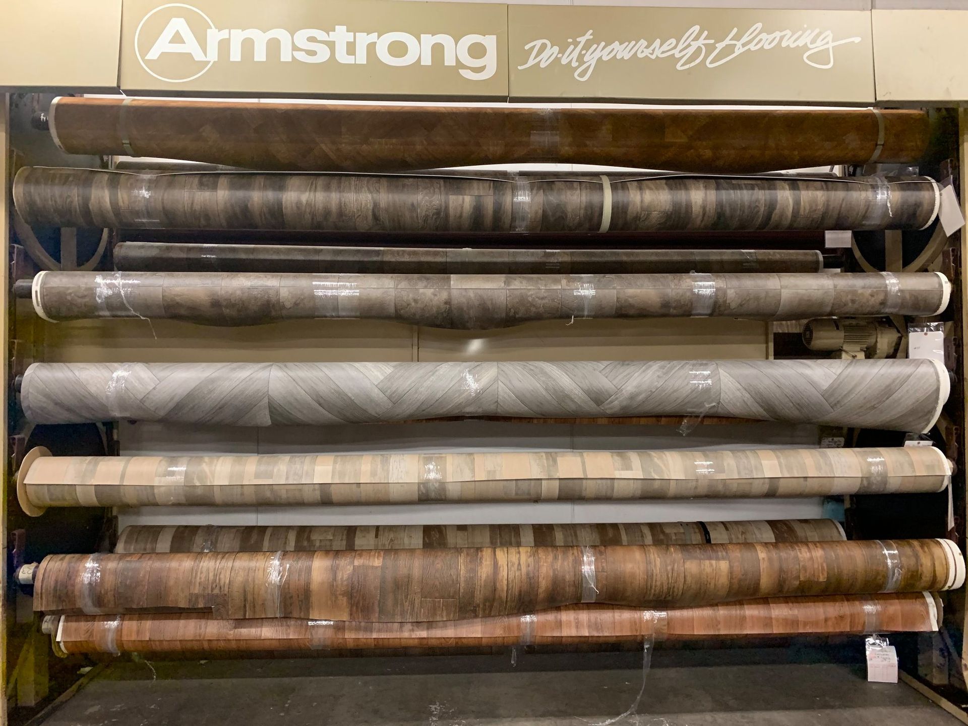 Display of Armstrong do-it-yourself flooring rolls in various wood-look patterns, stored in a retail fixture.