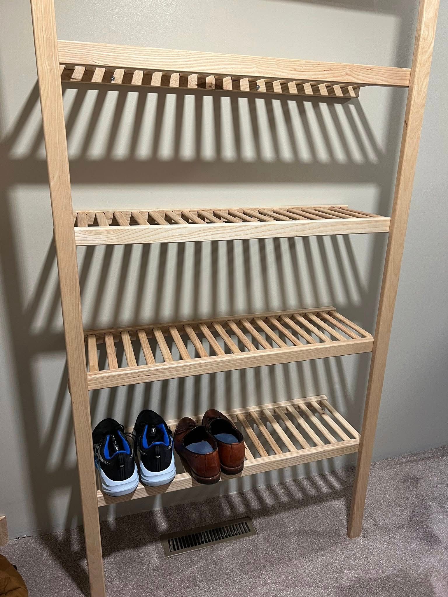 Wooden shoe rack with four shelves, holding three pairs of shoes.